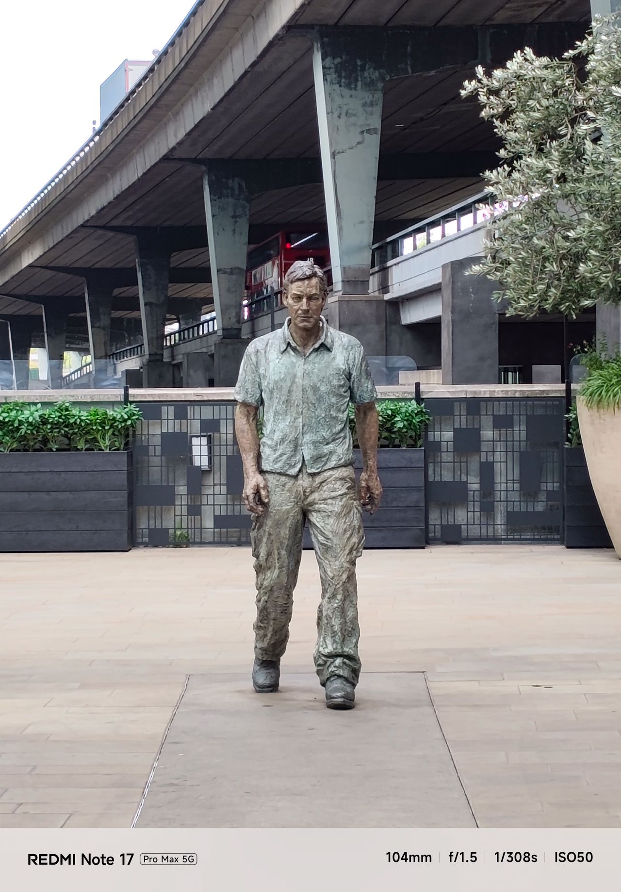 Close telephoto view of a walking man sculpture beneath an elevated roadway in London.