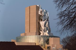 Rear view of twisting tower. The circular building below is covered in metallic panes and windows reflecting the evening light.
