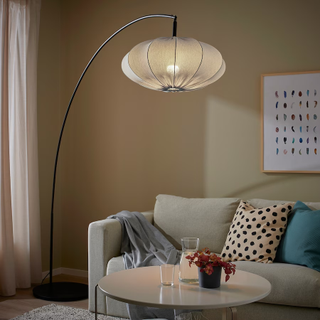 A living room with an arched floor lamp with a black base and a light blue textile shade overhanging the sofa