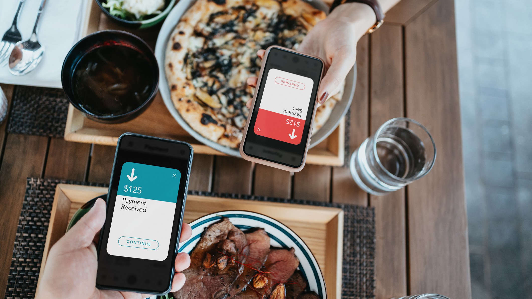 Friends splitting the bill while sending and receiving the payment of the meal through a digital wallet device on a smartphone while dining together in a restaurant
