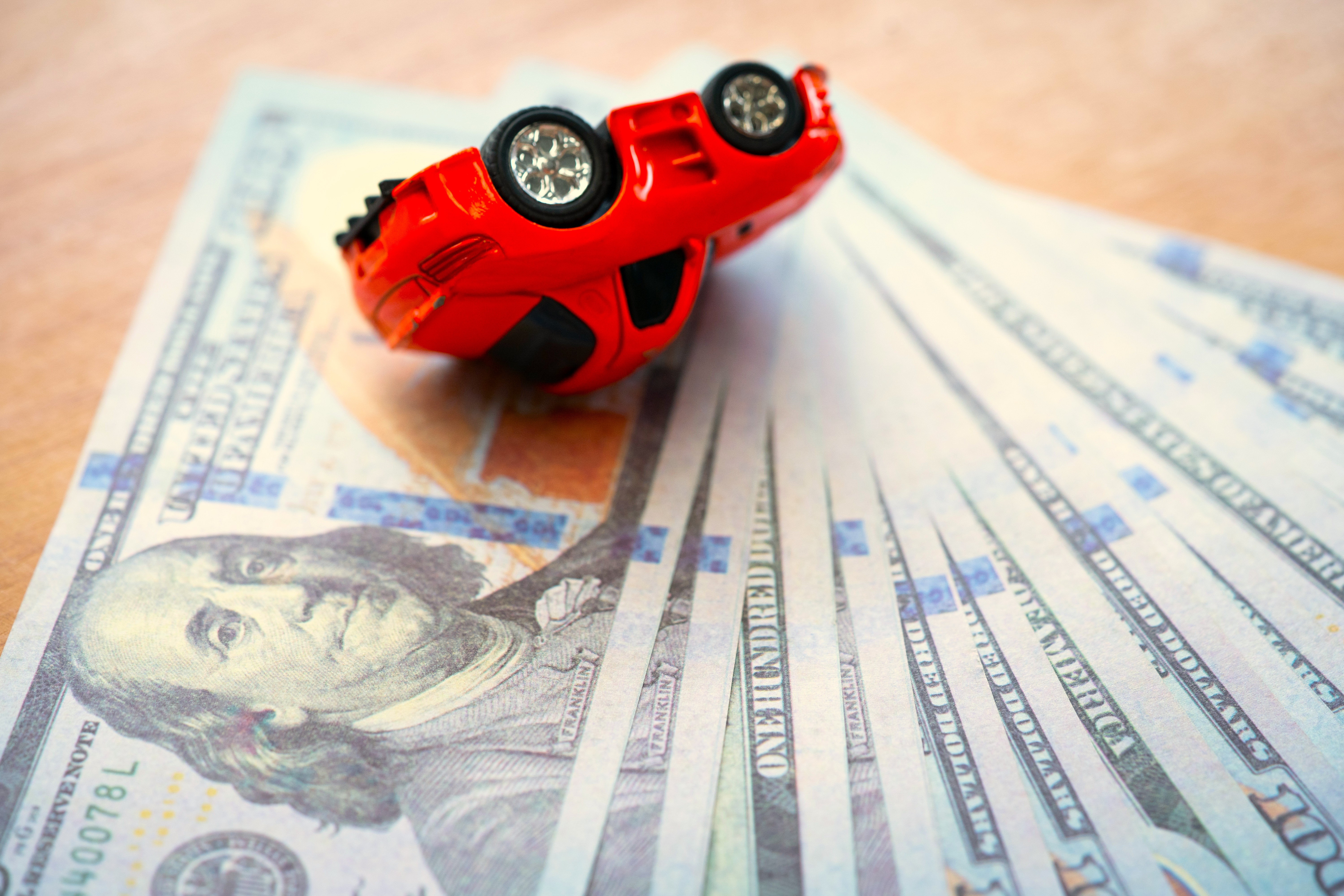 A toy car flipped over on top of a pile of $100 USD bills.
