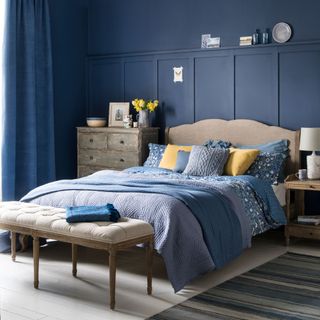 bedroom with blue wall cream colour bed with blue cushions wooden drawers