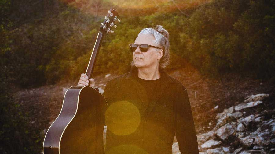 Andy Taylor holding an acoustic guitar in a garden