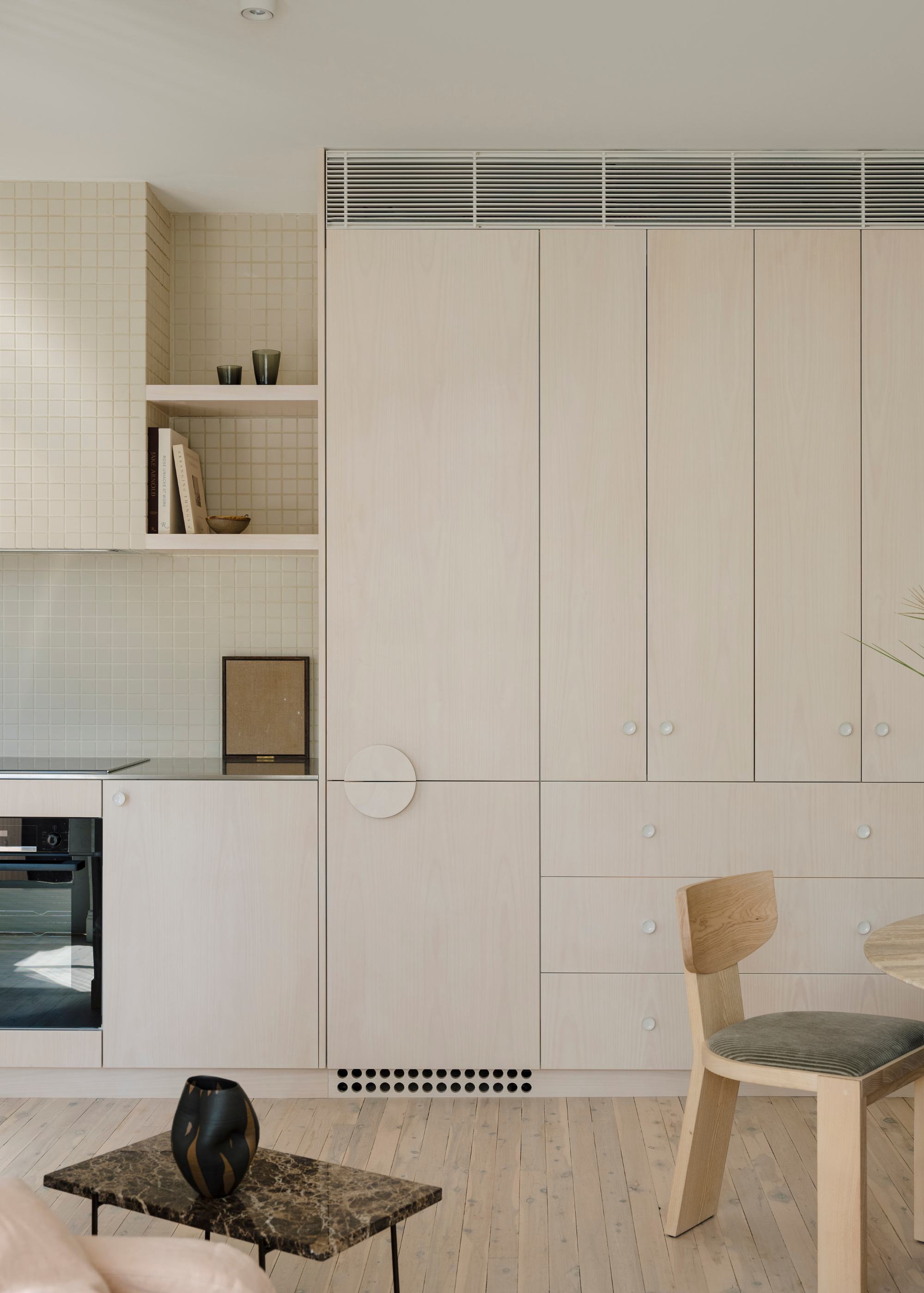 A light wood kitchen with a cupboard storage, a tiled backsplash, a stone side table and a vase