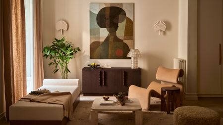 Living room with warm white walls, a mix of cream boucle and wood curved furniture, abstract figurative wall art, cream fan sconces and a neutral rug