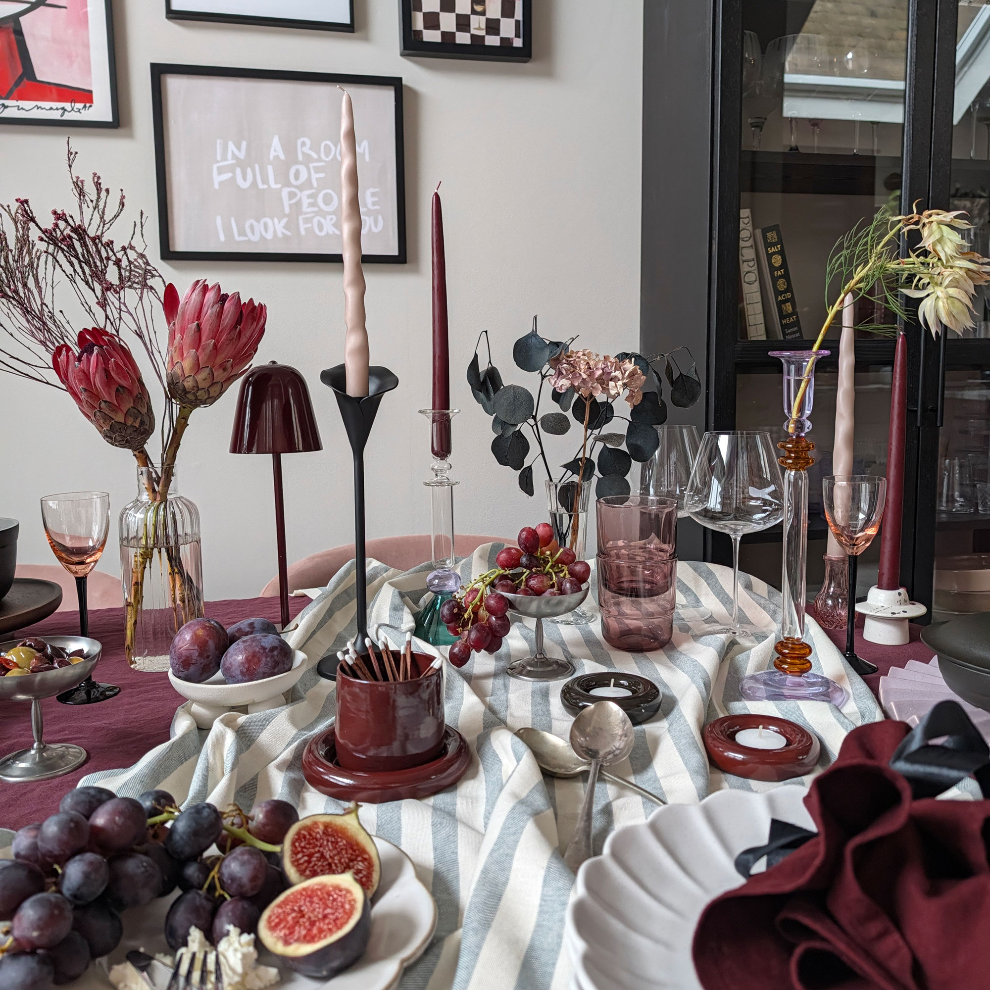 Table set for dinner party with striped tablecloth, glass and metal candlesticks, vases of flowers, bowls of fruit