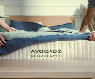 Hands pulling a duvet down over the Avocado Eco Organic Mattress.