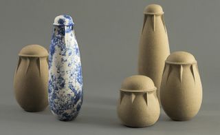 Grey floor and background, four beige stone and one blue and white design ceramic vessels on display