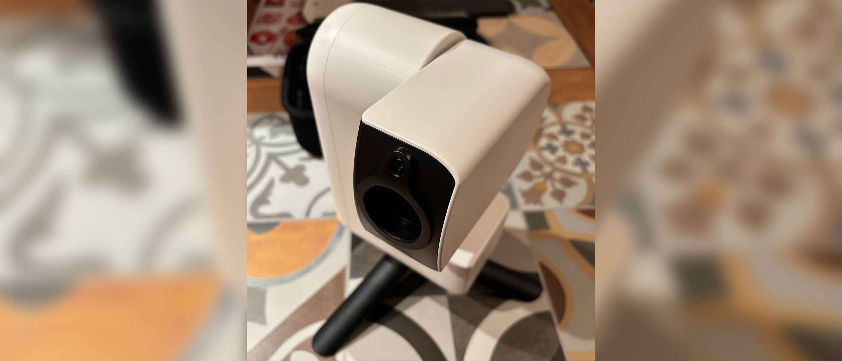 A white smart telescope with a black lens is standing on black legs on a tiled surface.