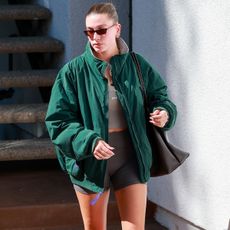 Hailey Bieber wears a green jacket, tan set active top, leggings, a black tote bag, socks, and black loafers.