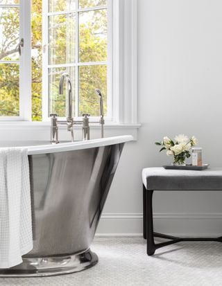 A shiny freestanding bathtub in front of a window