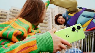 Kaupunkiympäristössä oleva tyttö pitää kädessään vaaleanvihreää OnePlus Nord CE 3 Lite 5G -puhelinta puhuessaan ystävälleen.