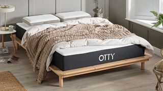 The best OTTY mattress discount codes, sales and deals: the Otty Original Hybrid Mattress on a light wooden bed frame and dressed with a white duvet and beige bed throw