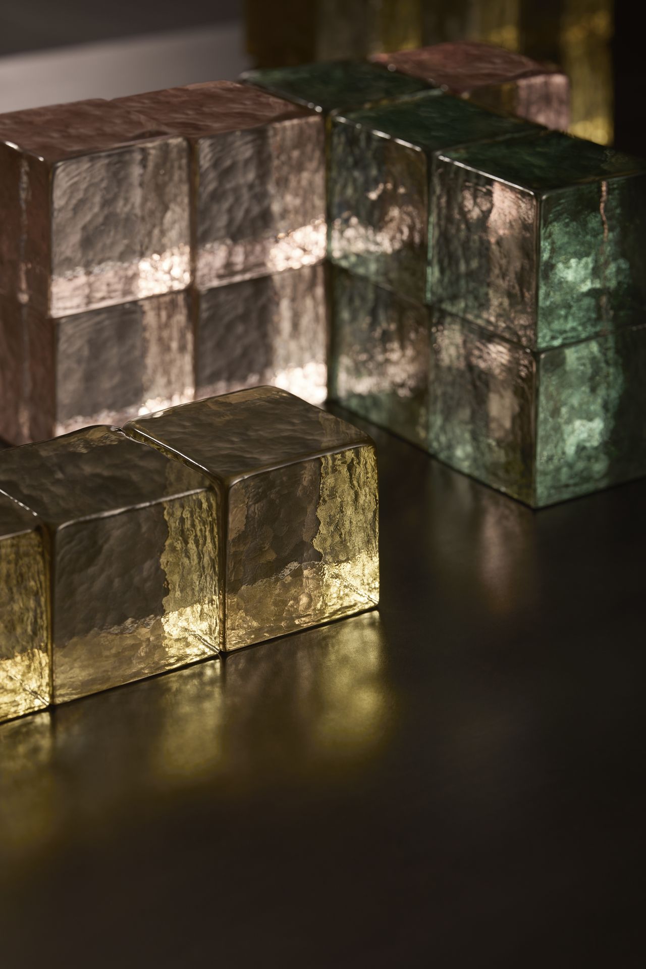 A series of cube-shaped lights in yellow, rose, and green sits on a wooden, bare surface.