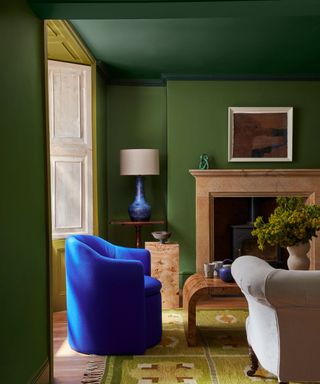 green painted living room, with large fireplace, blue armchair and green patterned rug