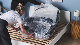 Two mattress testers unboxing a memory foam mattress that's wrapped in plastic onto a memory foam mattress