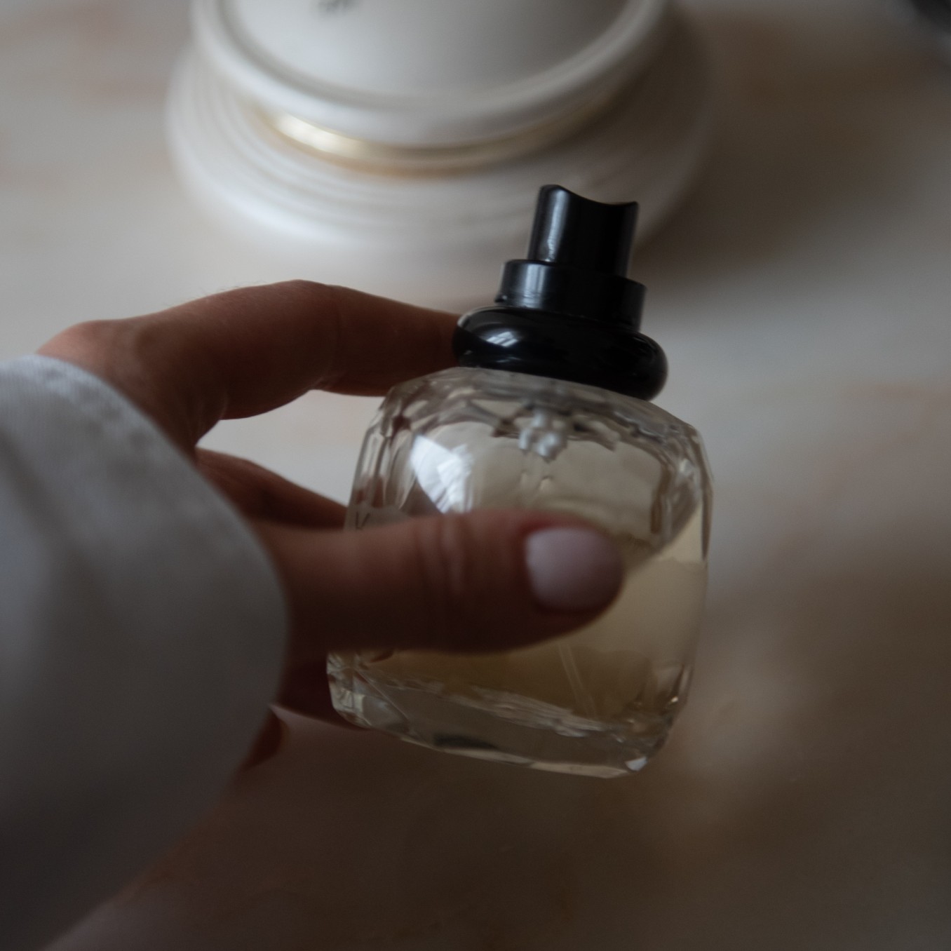 Hand holding clear perfume bottle with black spray atomizer