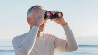 Man holding binoculars in front of the ocean