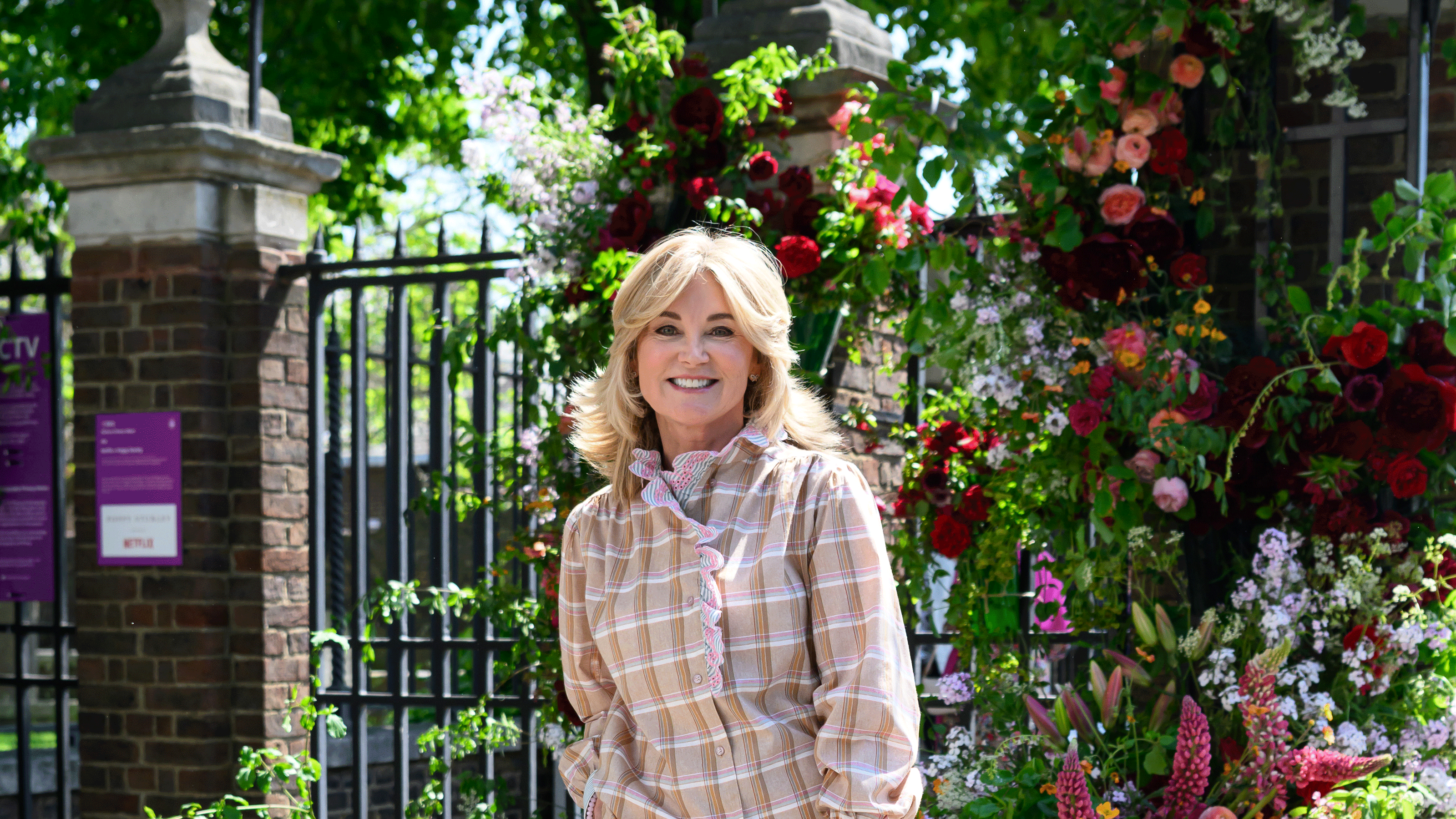 Anthea Turner in checked shirt with greenery behind her and the Chelsea flower show gate