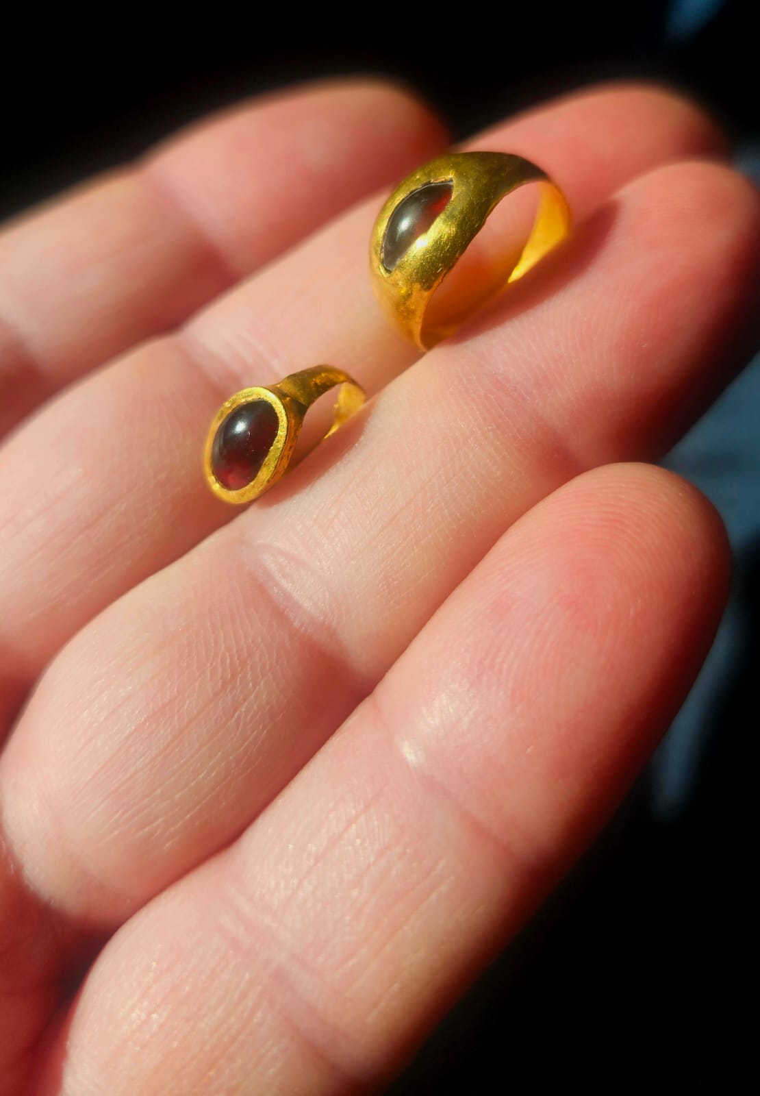 A person holds two gemstone gold rings that were found at the burial site.
