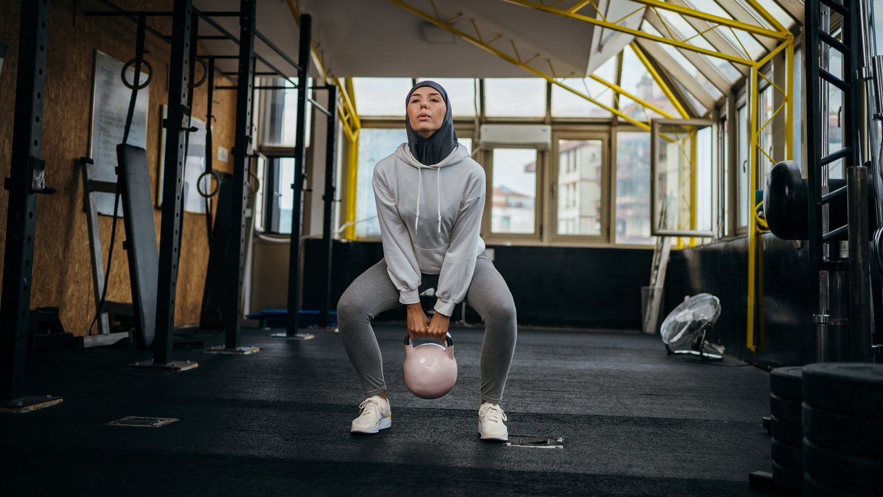 A woman in workout gear performs a sumo squat with a kettlebell