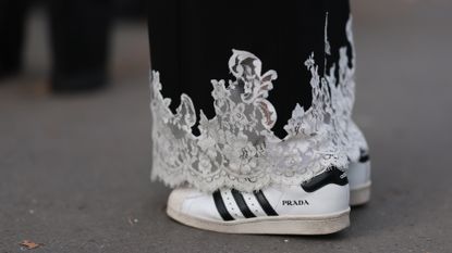 A woman at fashion week wears a pair of prada sneakers with a lace skirt