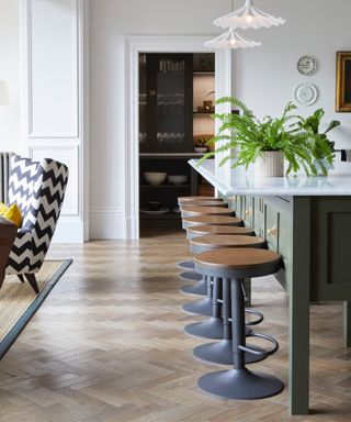 kitchen renovation rules, open plan kitchen with sage green island, bar stools, armchairs to left, fluted pendants, bar stools, view of pantry