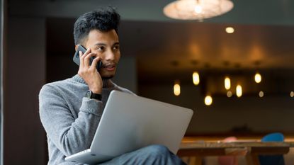 A young entrepreneur talks on the phone with a laptop on his knee.