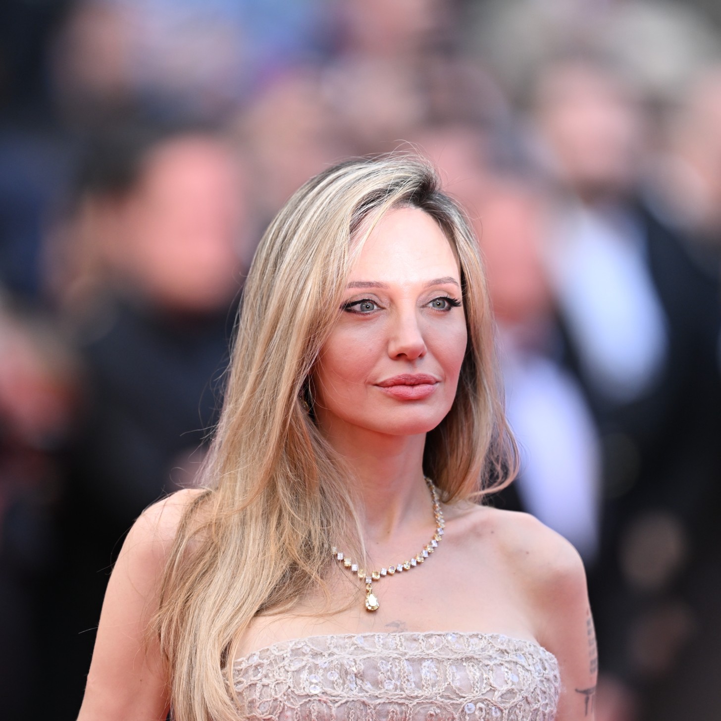 a woman with blonde hair photographed in front of a crowd of people on a red carpet