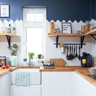 kitchen area with white units and wooden worktop and wooden shelves