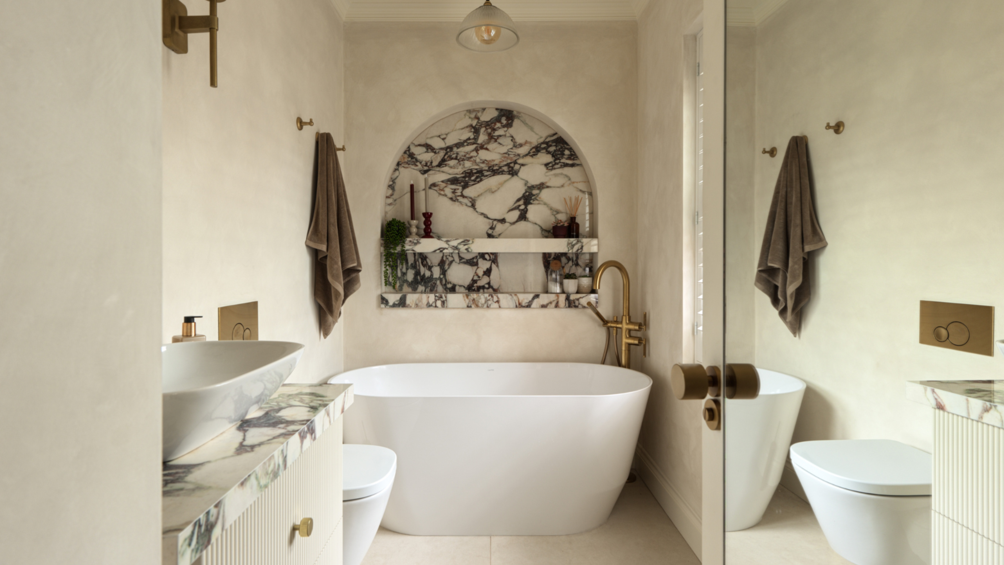 A spa-like neutral bathroom with a striking arched marble niche centred over the bathtub, next to a brown towel hanging high on the wall