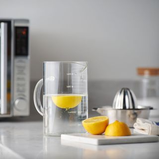 a jug of water with lemon on a worktop with a microwave in the background