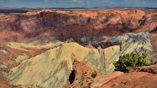 View from the edge of Upheaval Dome in Utah. We see a steep sandstone outcrop surrounding a central, whitish outcrop.