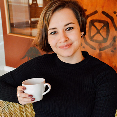 Tara Spaulding sat on a sofa wearing a black turtleneck jumper holding a mug of coffee.