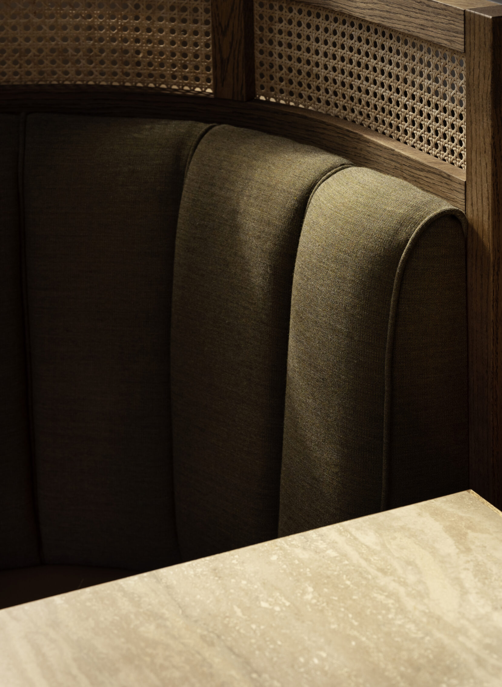 A sophisticated, retro-inspired restaurant with wood paneled walls, dark green upholstered banquettes, glazed golden tiles placed atop patterned black and white fabrics, and sculptural lights.