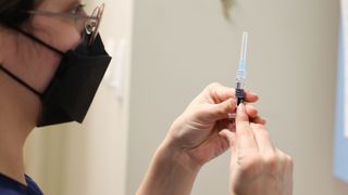 woman wearing glasses and a black kn95 mask prepares a syringe to deliver a flu shot