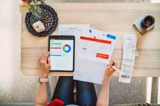 A woman using a budgeting app on her tablet sitting at a desk. 