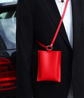 Close up image of a person in a black blazer and white shirt wearing a cross body red handbag, black car backdrop, car back light