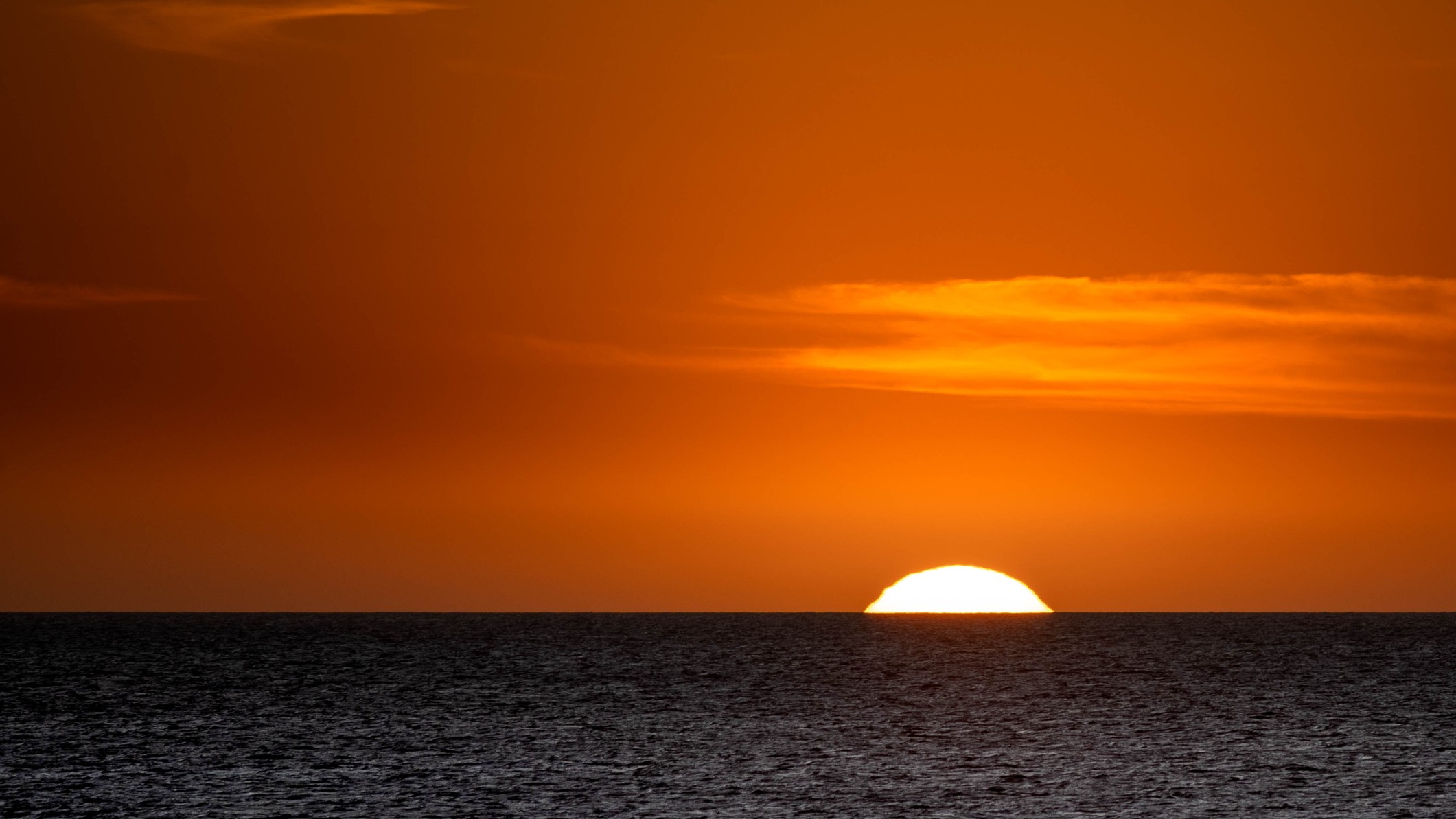 sunset with deep orange sky, the sun is just appearing above the horizon.