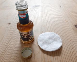 a bottle of vanilla extract open next to a cotton round on a wooden table