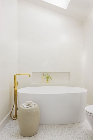 white bathtub with gold hardware and cream stool