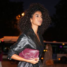 Imaan Hammam is seen wearing a long black coat, tan heels and holding a burgundy handbag