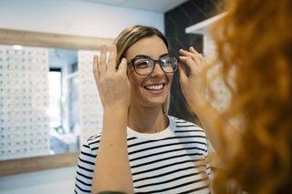 woman in striped top smiling as she is trying on glasses in an opticians