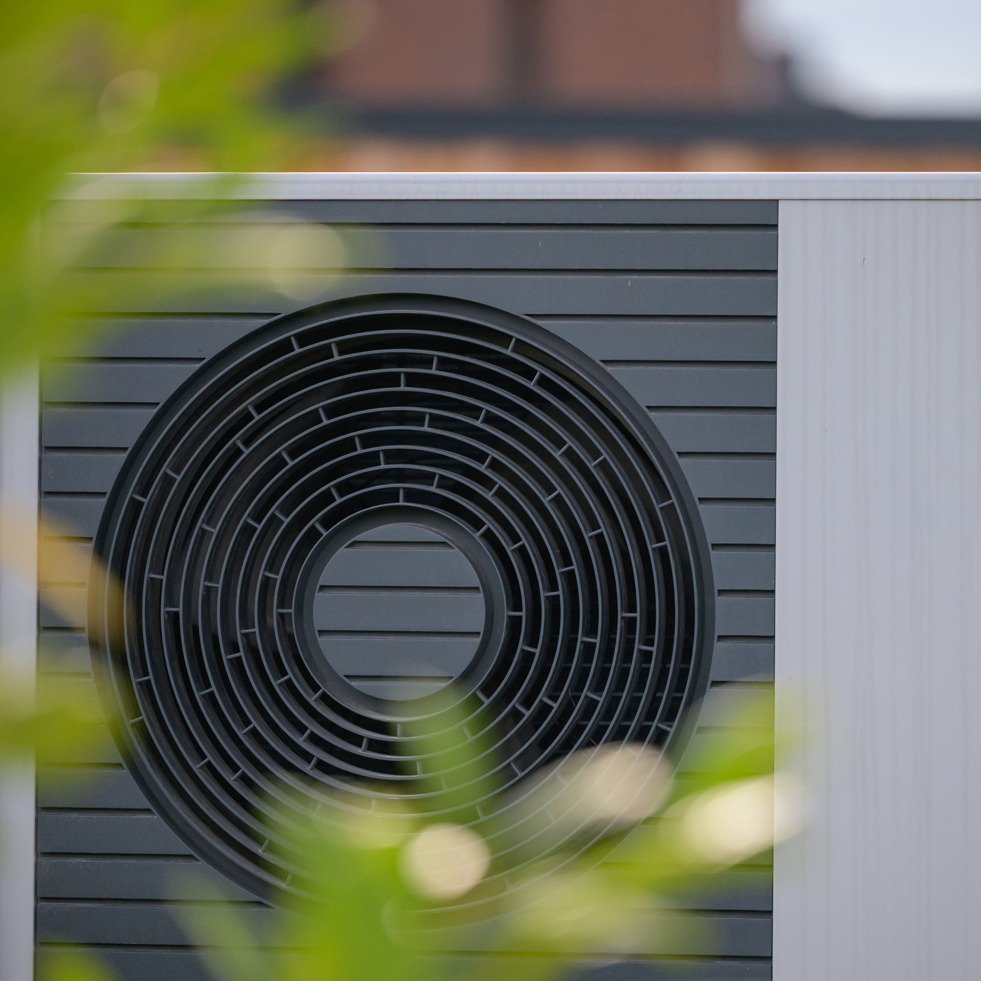 Close up of an air source heat pump through some leaves
