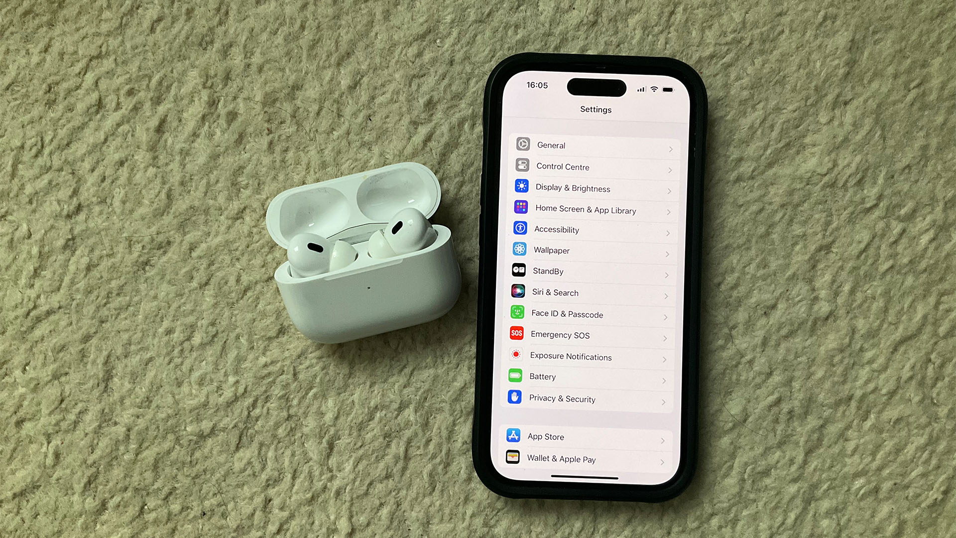 An Apple iPhone next to some AirPods. The iPhone displays the Siri settings.
