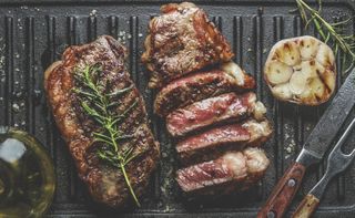 Close up of sliced roasted medium rare barbecue steak with rosemary, roasted garlic and cutlery on rustic iron grill.
