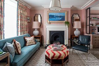 Window treatment idea with floor to ceiling curtains behind a blue sofa in pink living room