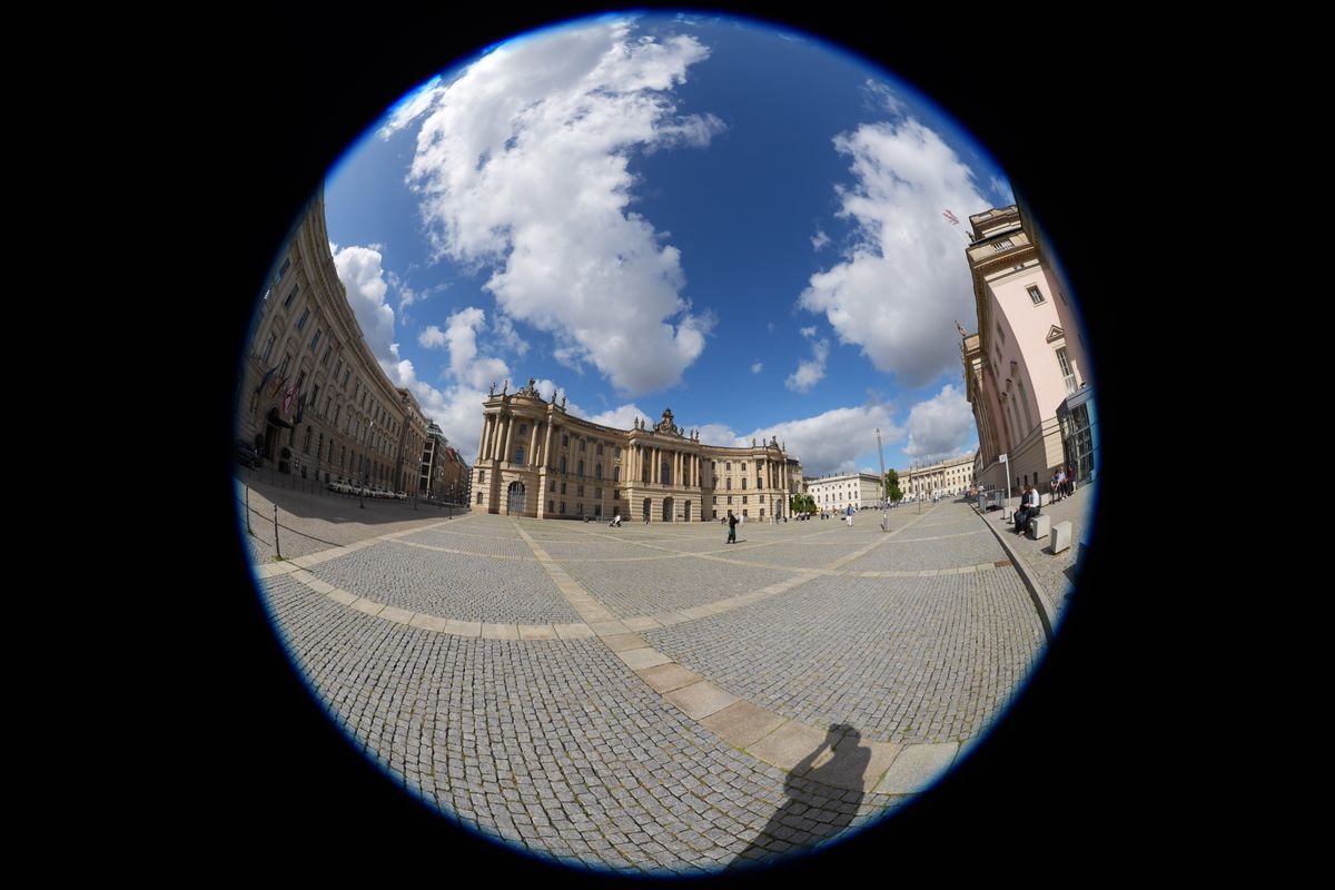 Circular fisheye view across a large historic square in central Berlin, surrounded by classical buildings under a cloudy blue sky.