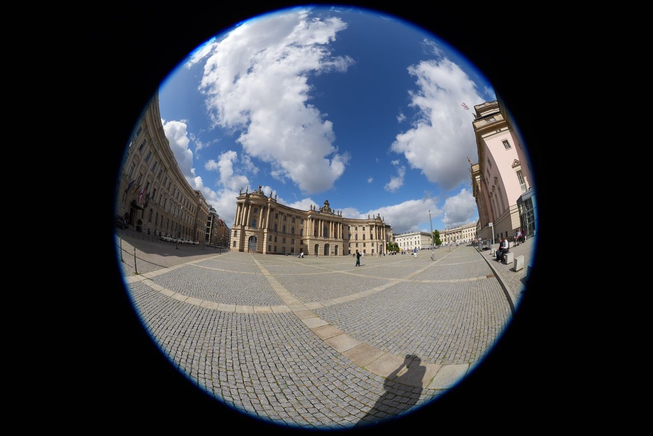 Circular fisheye view across a large historic square in central Berlin, surrounded by classical buildings under a cloudy blue sky.