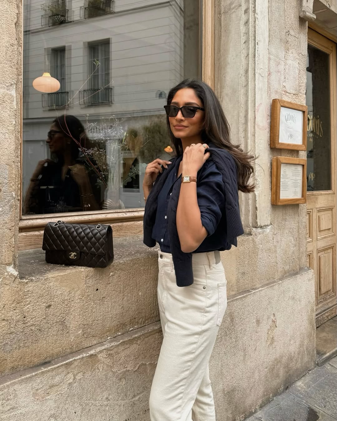 @cocobeautea carries a black Chanel bag whilst wearing a navy shirt, navy cardigan and cream jeans